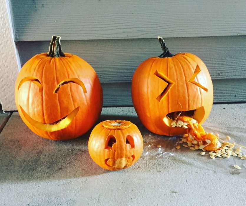 Three carved pumpkins: one smiling, a small one shocked, and a third vomiting seeds and pulp.