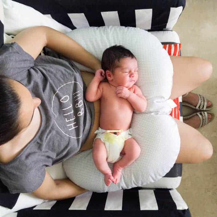A newborn baby sleeping on a nursing pillow across a woman’s lap.