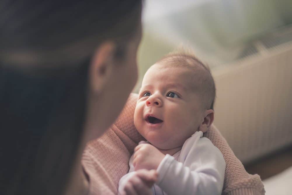 A smiling infant being held and looking up at an adult.