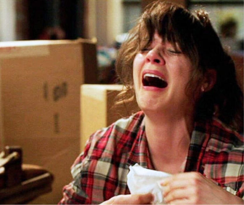 A woman in a red plaid shirt cries with her mouth wide open while holding a crumpled tissue.