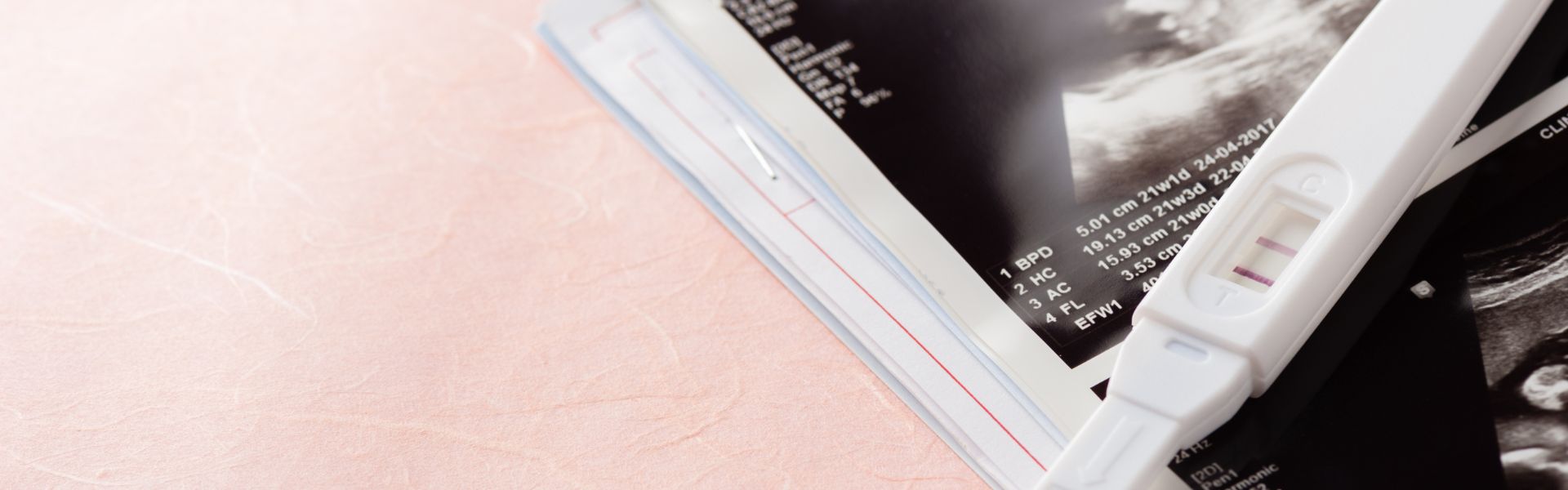 Positive pregnancy test lying on top of black and white ultrasound printouts.