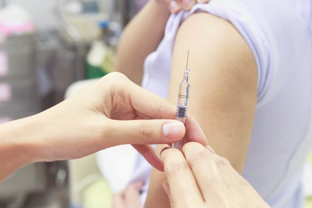 Close-up of a healthcare provider holding a syringe to administer a vaccine into a patient's upper arm.