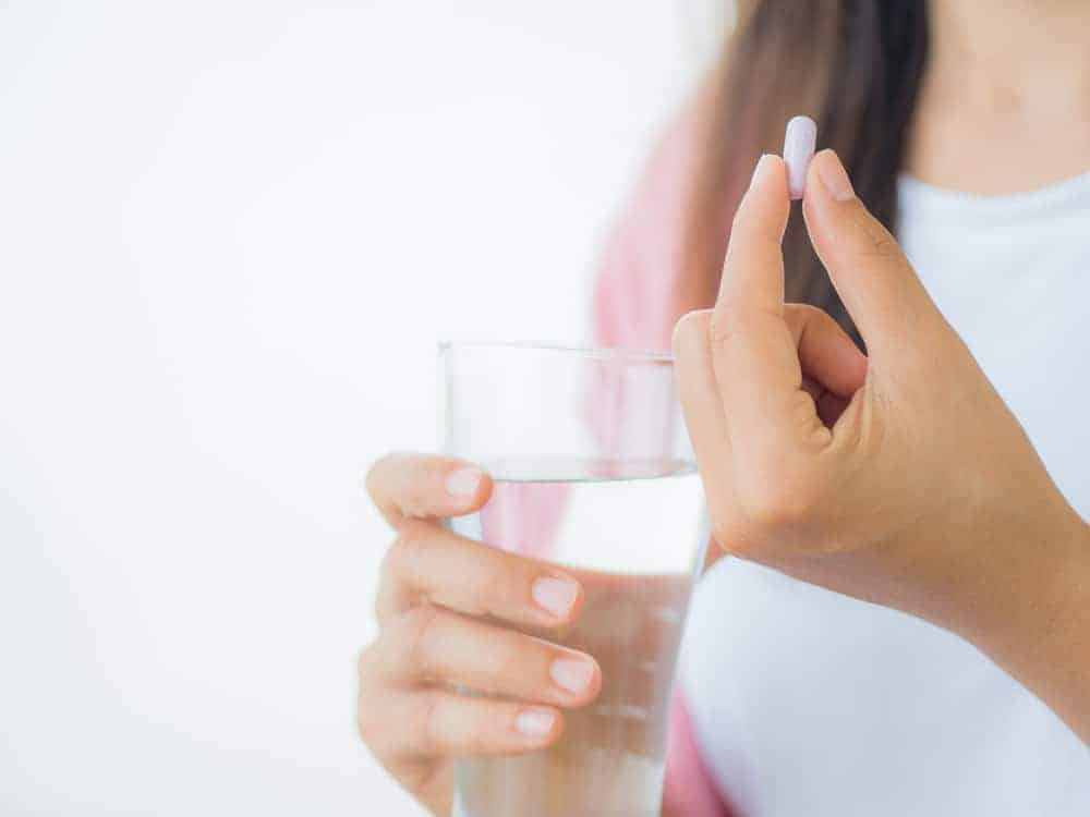 Close-up of a person's hands holding a glass of water and a small pink folic acid pill.