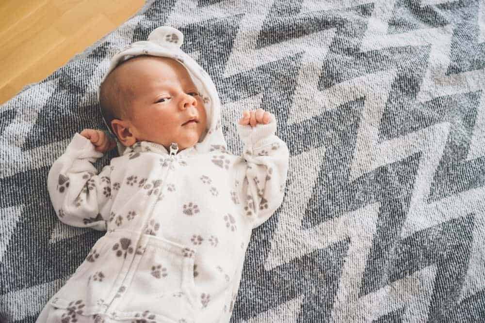 Newborn baby in a paw-print hooded onesie lying on a grey and white chevron patterned blanket.