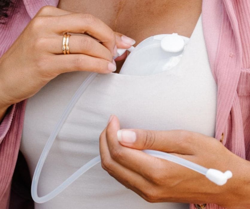 Close-up of a person tucking a wearable breast pump into a white bra under a pink shirt.