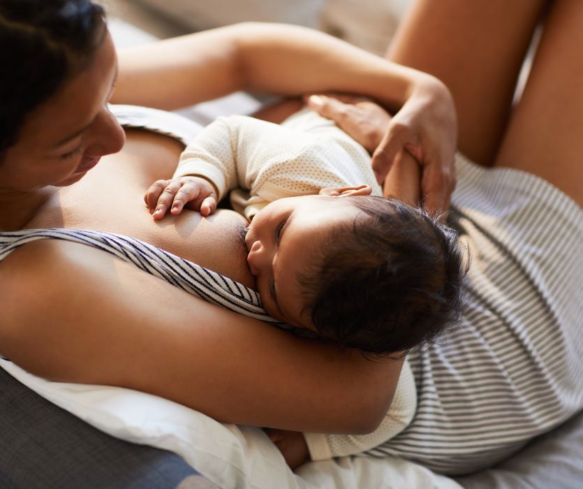 A woman cradle-holding and breastfeeding a baby while sitting down.