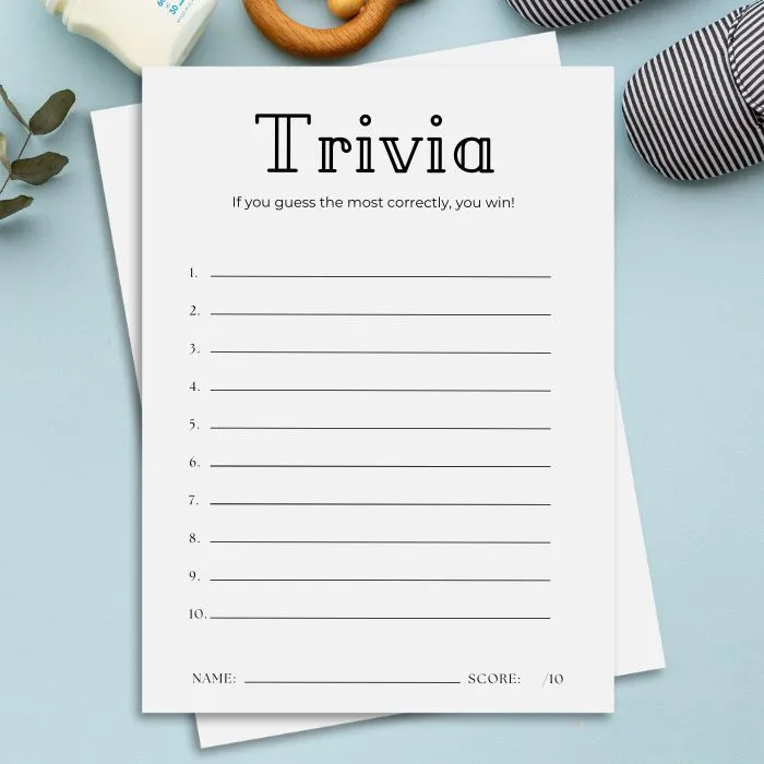Printed trivia sheet with 10 numbered blank lines on a blue surface surrounded by baby items.