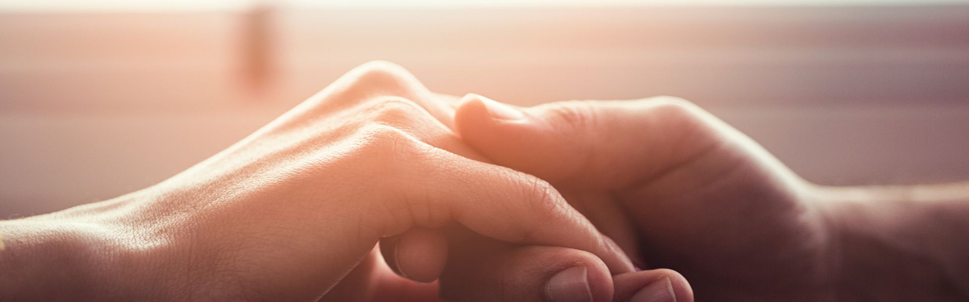 Close-up of two people holding hands in warm, soft lighting.