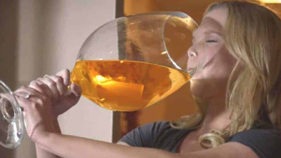 Amy Schumer drinks from an oversized wine glass filled with an orange liquid.