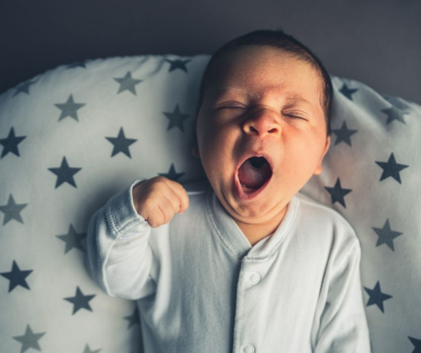 Newborn baby yawning while lying on a star-patterned pillow.