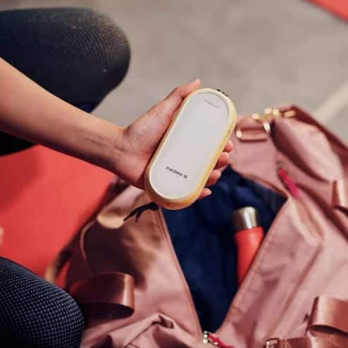 A person holds a small, oval-shaped Medela breast pump over an open pink gym bag.