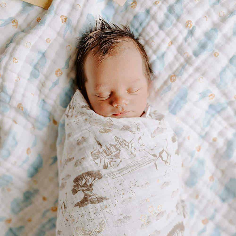 Sleeping newborn swaddled in a Harry Potter themed muslin blanket featuring Hogwarts castle and the Whomping Willow.