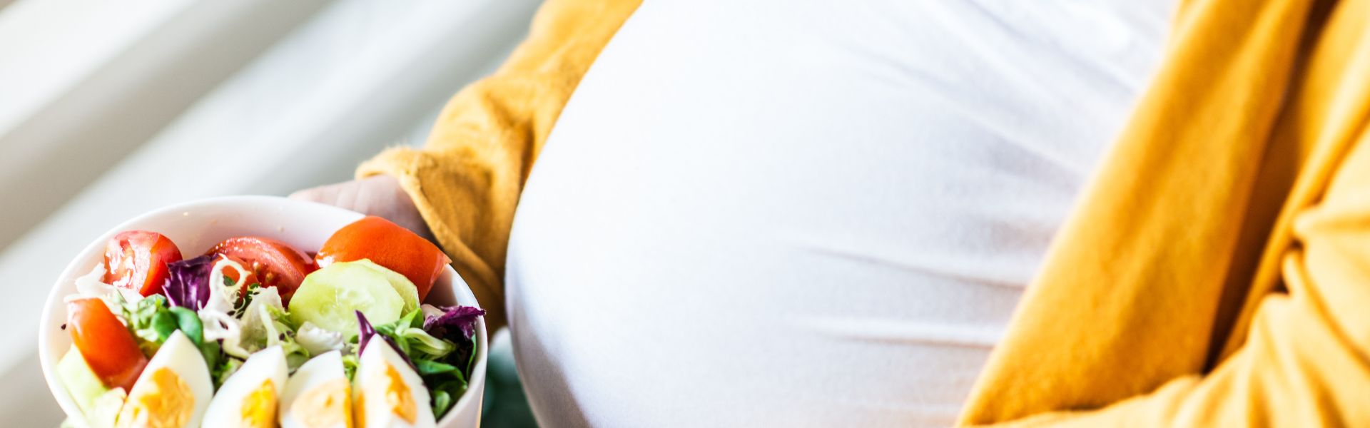 A pregnant person holding a fresh salad bowl with tomatoes, eggs, and greens.
