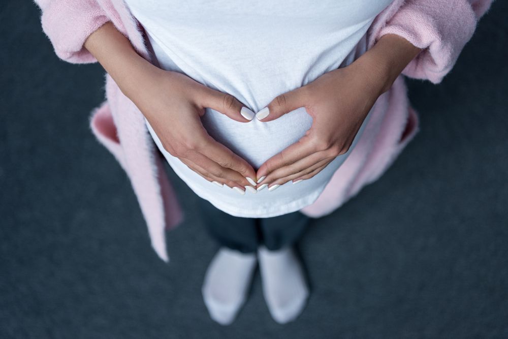 Looking down at a person making a heart shape with their hands over their stomach.