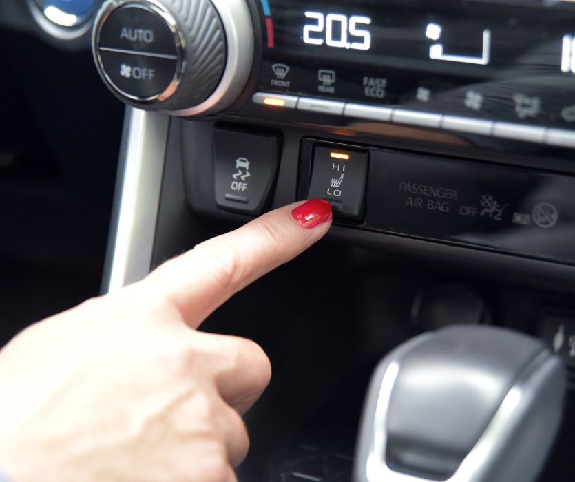 A finger with red nail polish pressing the high setting for a heated seat on a car's center console.