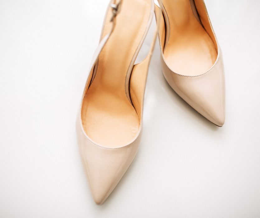 A pair of beige pointed-toe slingback high-heeled shoes on a white surface.