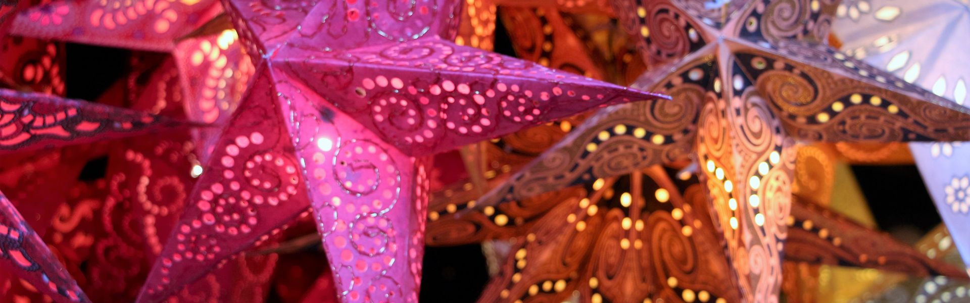 Close-up of pink, orange, and white illuminated paper star lanterns with intricate cutout patterns.