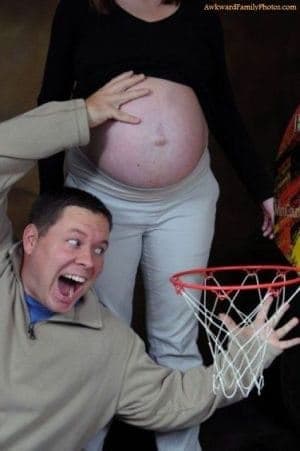 A man holding a basketball hoop below a woman's bare pregnant stomach as if she is about to dunk it.