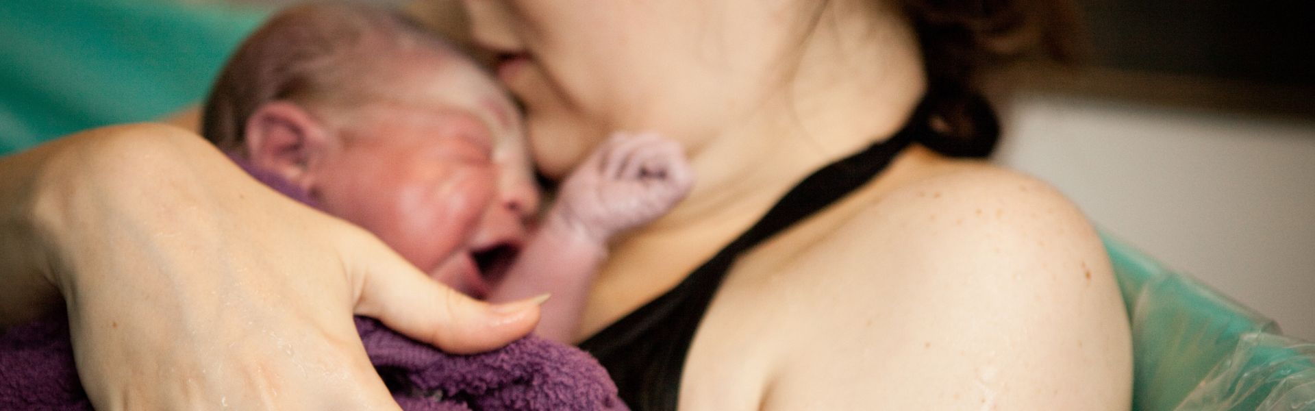A person holding a crying newborn baby during a water birth.