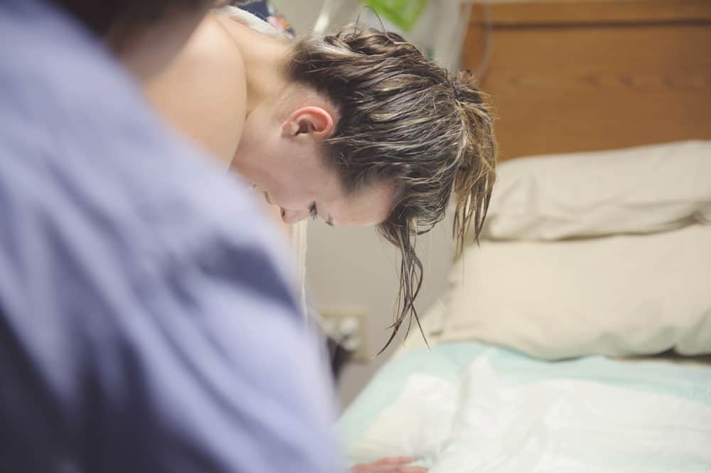 A woman with wet hair leans forward during labor in a hospital room.