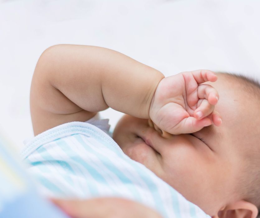 Close-up of a sleeping baby rubbing their eyes with one hand.
