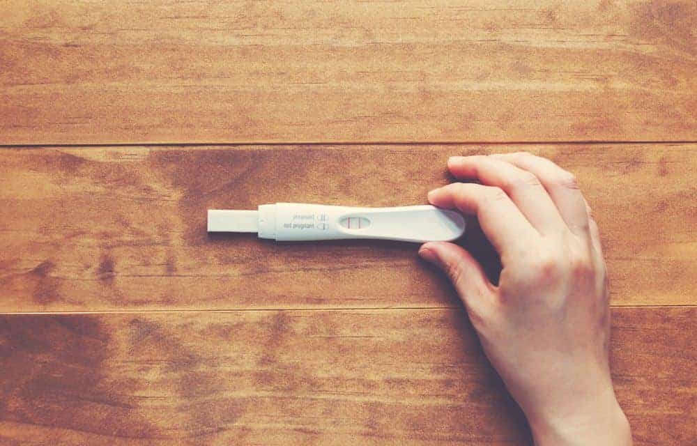 A hand holds a positive home pregnancy test showing two blue lines on a wooden surface.