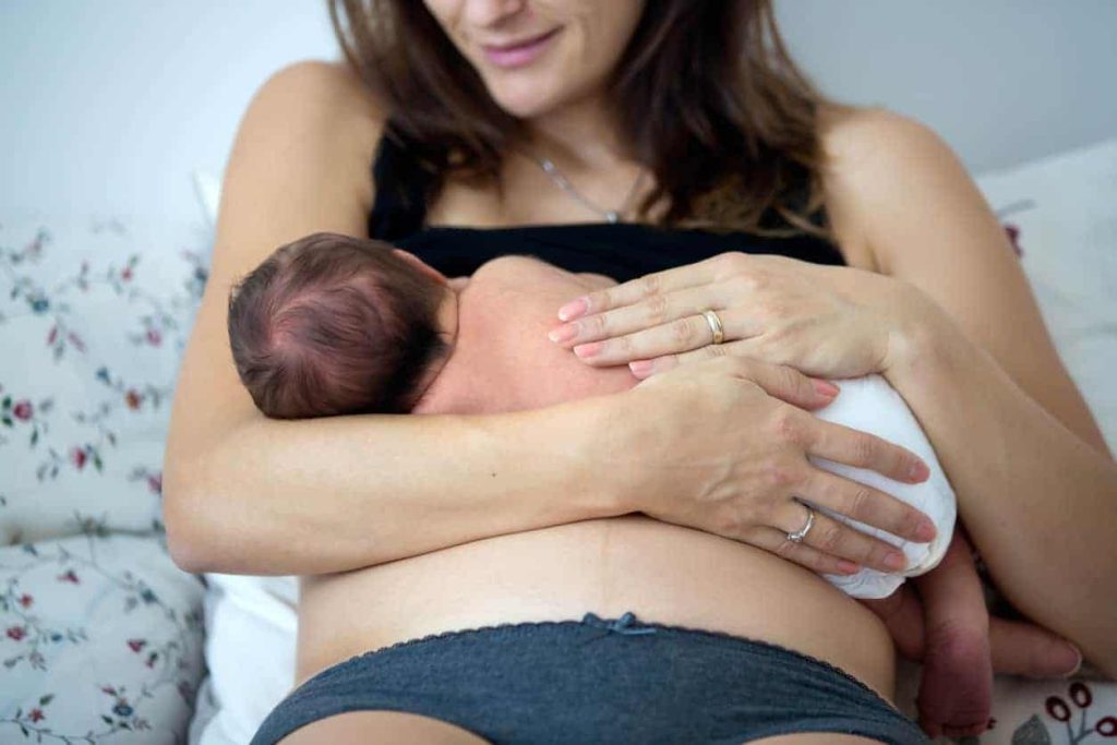 A mother breastfeeding her newborn infant while sitting on a floral patterned bed.