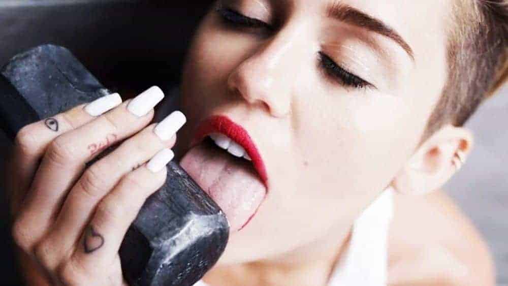 A woman with red lipstick licks a dark block of chalk in close-up, reflecting pregnancy pica cravings for dirt, chalk, or other non-food items.