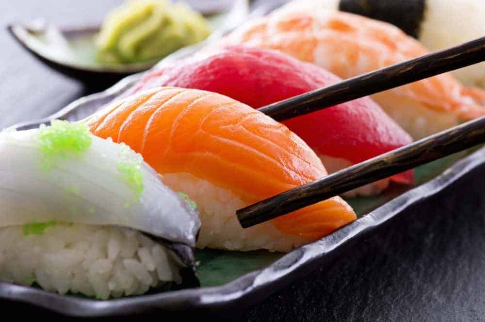 Raw salmon nigiri sits on a dark plate with chopsticks, alongside other sushi pieces and wasabi, echoing the question of sushi while pregnant.