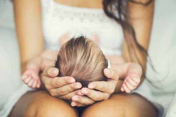 A woman cradling a newborn baby’s head in her hands as the infant rests on her lap.