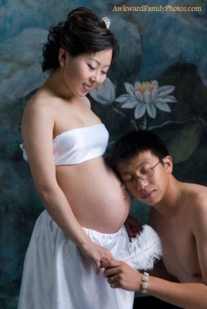 A man rests his head against a pregnant woman's belly while holding a white feather against the backdrop of a lotus mural.