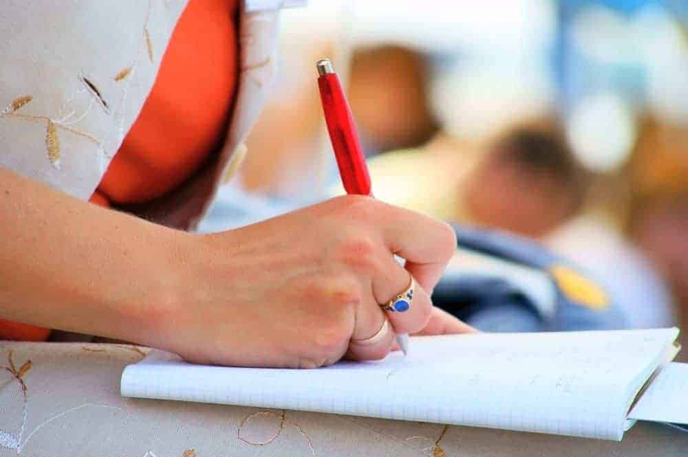 A person's hand writing in a notebook with a red pen.