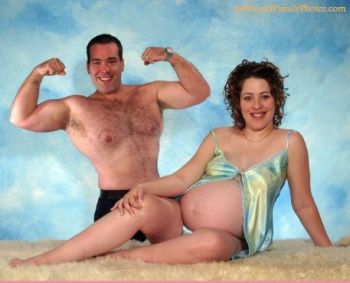 Shirtless man flexing his muscles behind a pregnant woman sitting on a white rug against a blue backdrop.