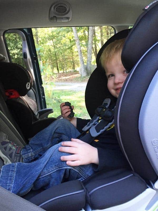 A young boy strapped into a rear-facing car seat inside a vehicle, holding a small toy.