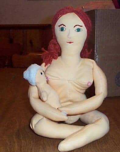 Handmade cloth doll with red yarn hair breastfeeding a smaller infant doll in a blue hat.