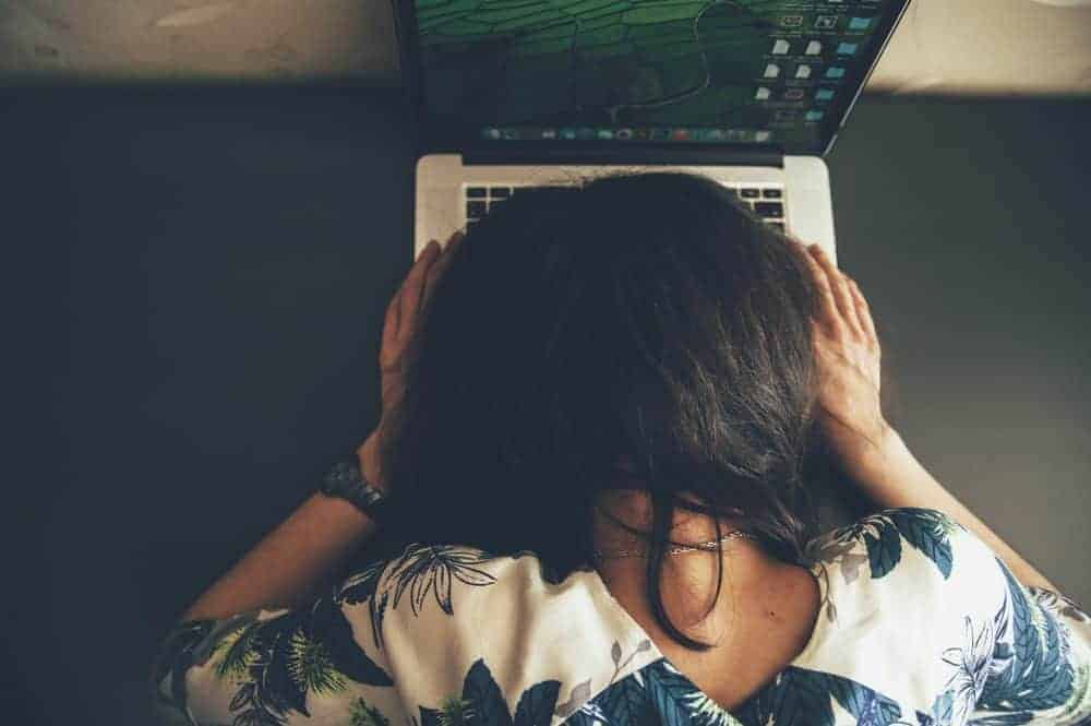 Overhead view of a person with dark hair holding their head in their hands while looking down at a laptop.