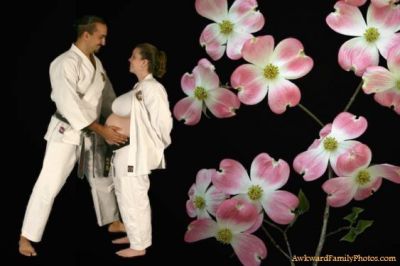 Man in karate gi touches the stomach of a pregnant woman in a karate gi next to pink flowers on a black background.