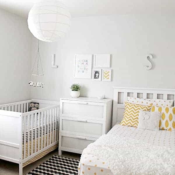 White nursery with a crib, dresser, and bed featuring yellow and white patterned pillows and wall-mounted initials.