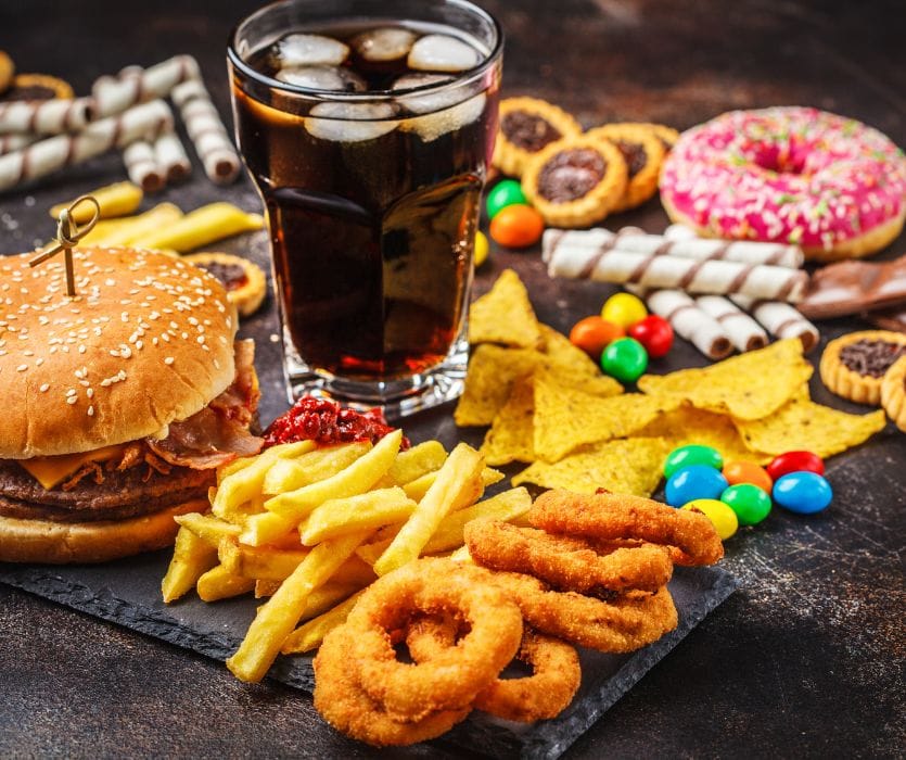 A burger, fries, onion rings, soda, chips, candy, and a donut spread across a dark table.