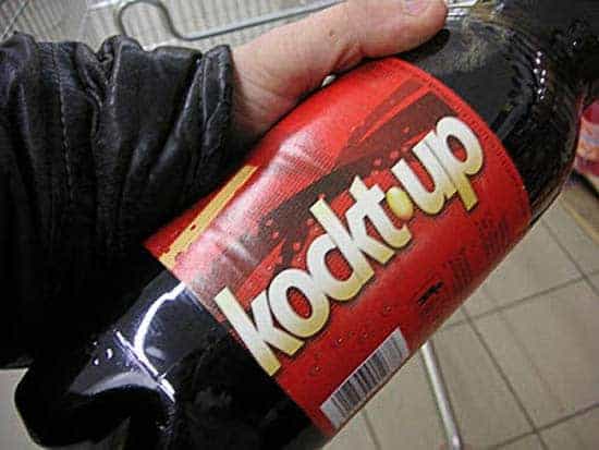 A hand holding a plastic bottle of dark soda with a red label that reads Kockt.up in white and yellow letters.