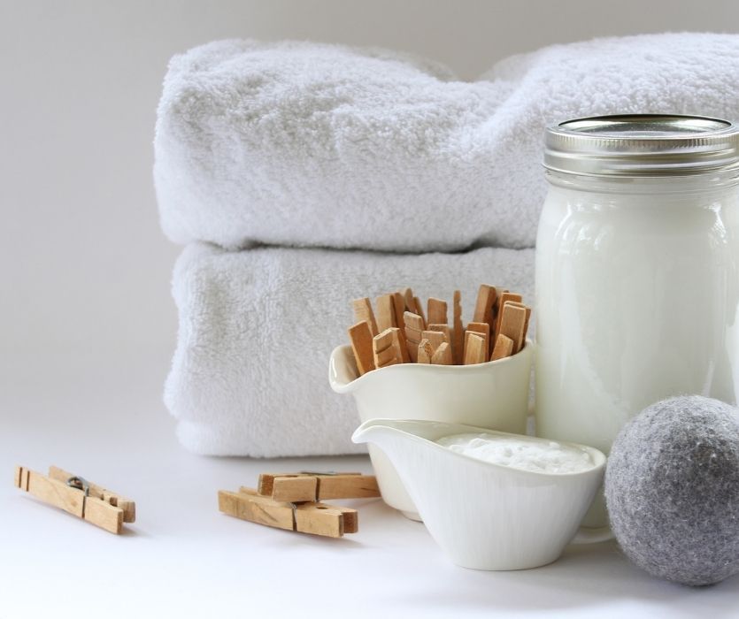 Two folded white towels, wooden clothespins, a mason jar of detergent, and a wool dryer ball.
