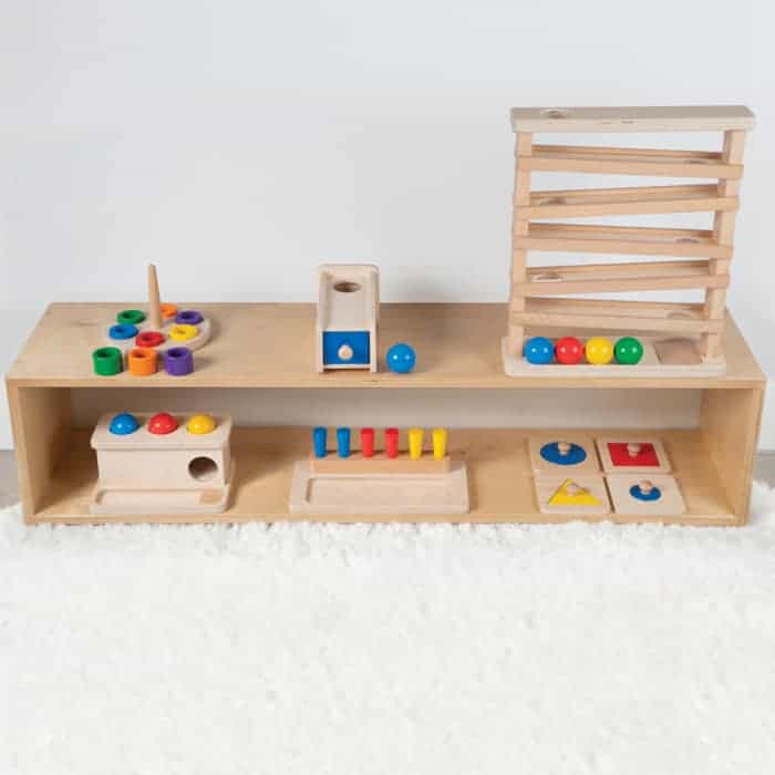 Wooden Montessori educational toys, including a ball run, ring stacker, and puzzles, arranged on a light wood shelf.