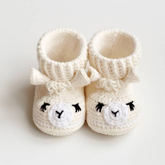Cream crocheted baby booties featuring a llama face with embroidered eyes and ears.