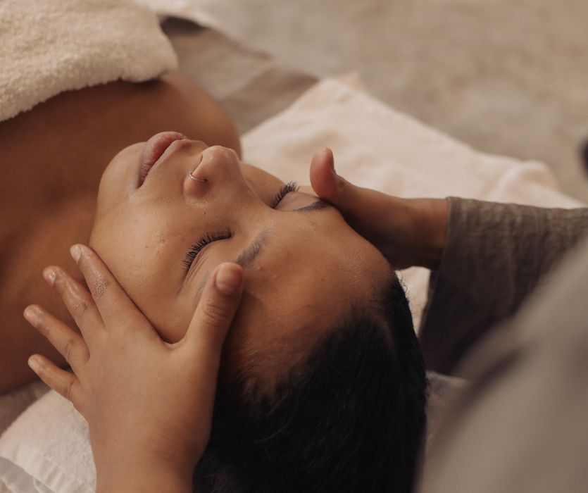 Close-up of a person with eyes closed receiving a facial massage from a therapist.
