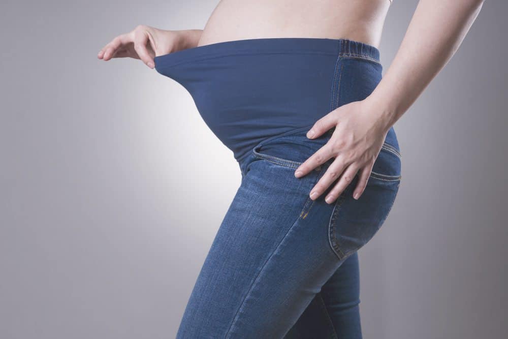 A pregnant person wearing blue maternity jeans with a stretchy navy blue over-the-belly waistband.