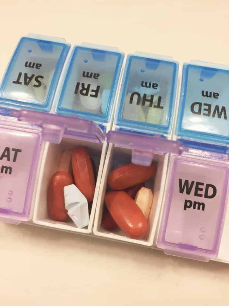 Several large orange pills and a white pill in an open weekly pill organizer.