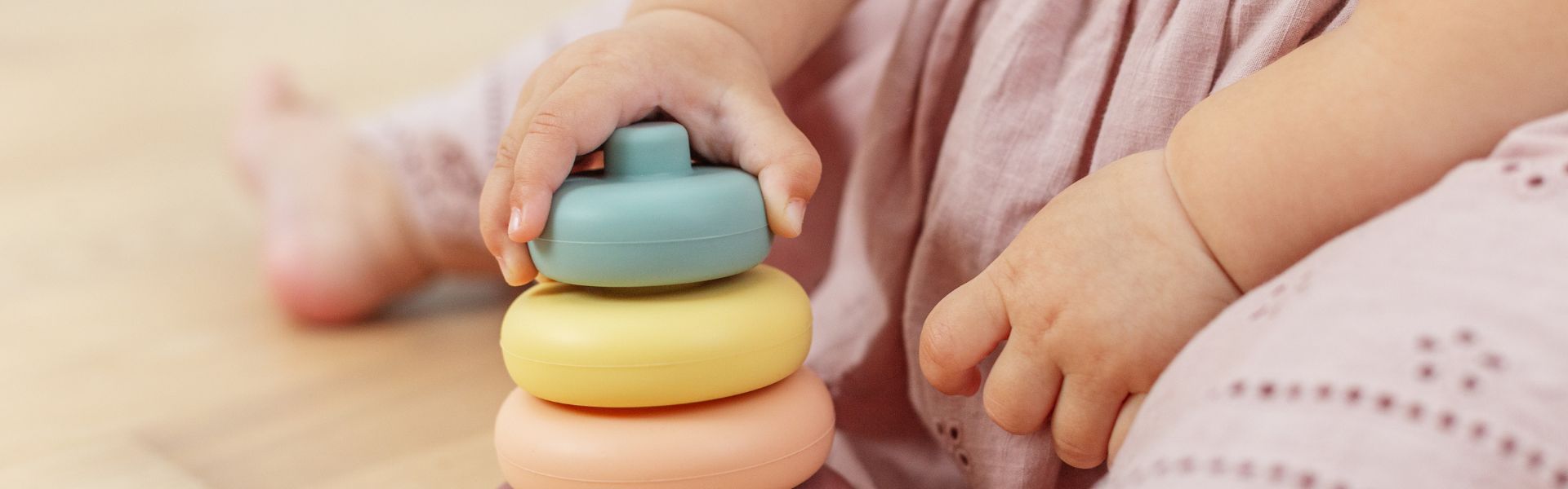 Close-up of a baby's hands stacking colorful silicone rings on a toy base.