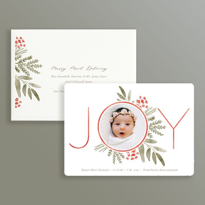 Holiday birth announcement featuring a newborn photo inside a JOY graphic with watercolor botanical accents.