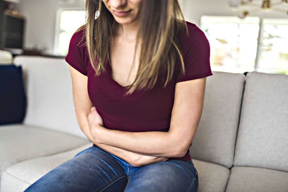 A woman sitting on a sofa and holding her abdomen in pain.