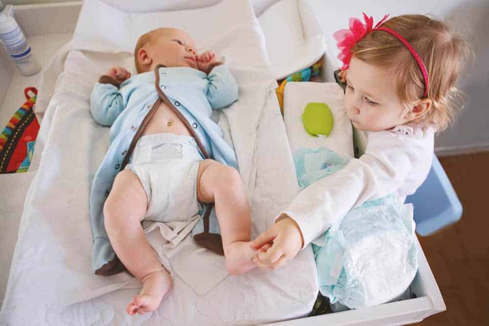 Young girl touching newborn brother's foot while he lies on a changing table.